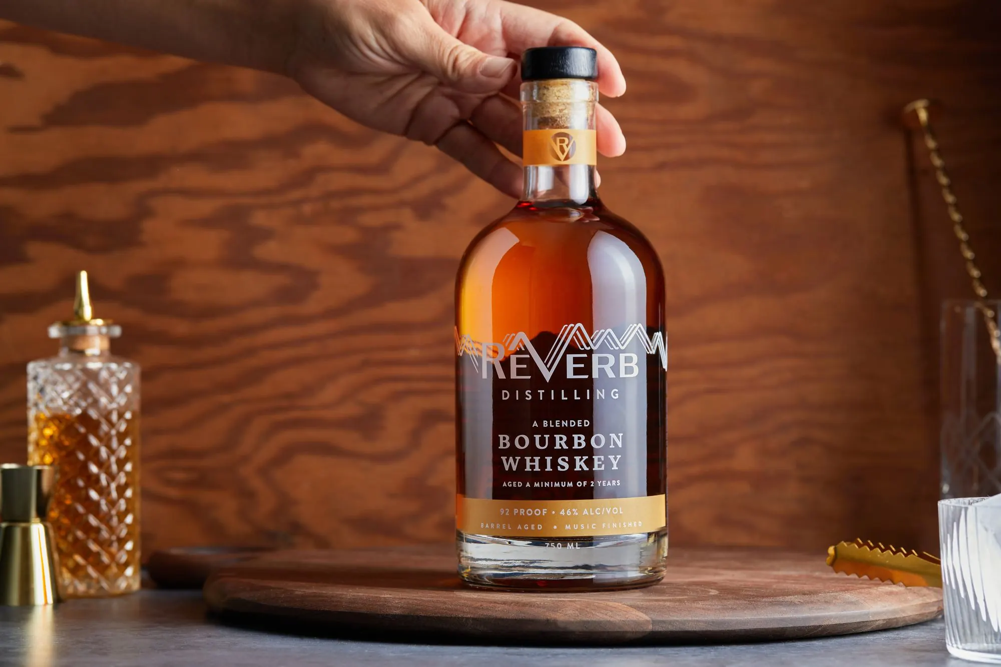 A hand setting a bottle of ReVerb Bourbon on a wooden tray