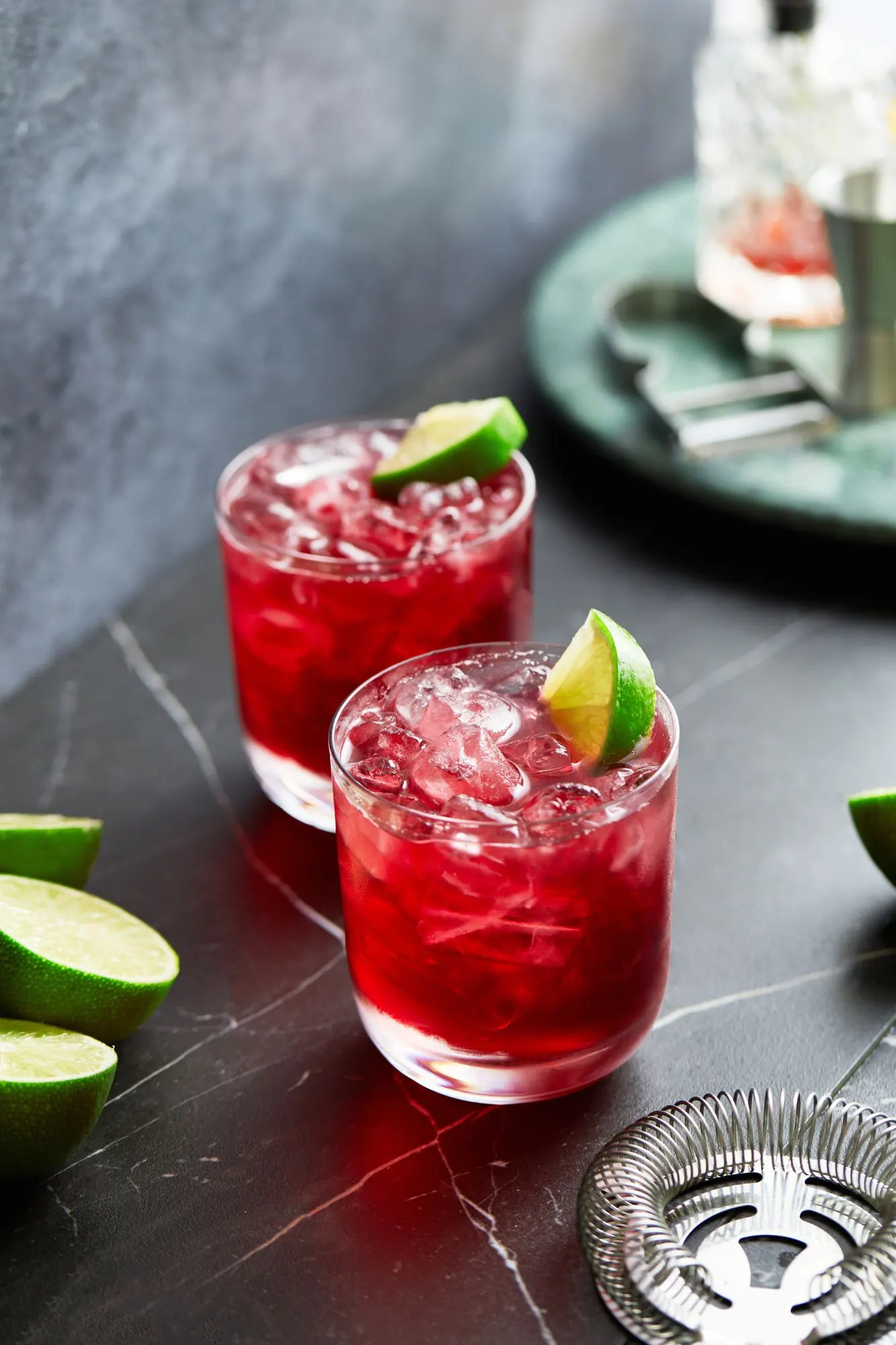 Two red hibiscus gin spritzes with lime beside ReVerb Gin