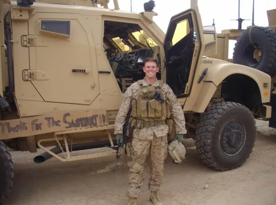 A Marine beside an armored vehicle with a hand-lettered thank-you sign