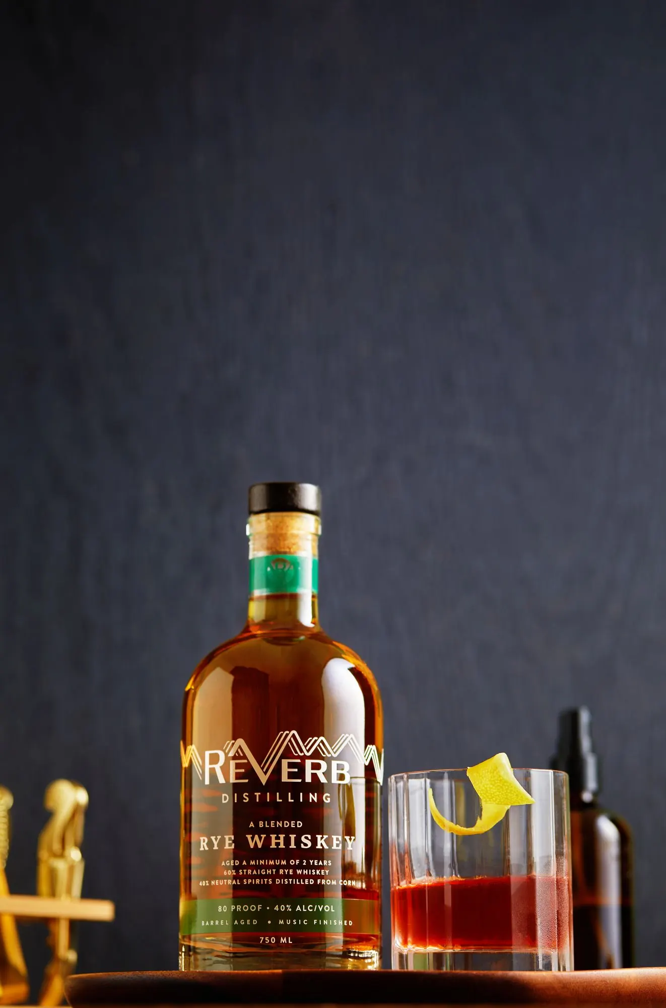 A ReVerb Rye cocktail with lemon beside the bottle